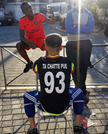 a man wearing a fly emirates shirt sits next to a man wearing a 93 jersey