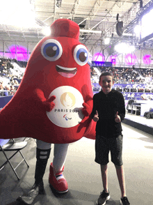 a boy is standing next to a mascot for the paris paralympic games