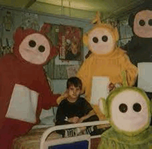 a child is sitting in a hospital bed surrounded by teletubbies costumes .