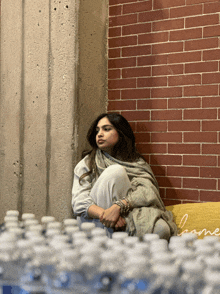 a woman sits on a couch in front of a brick wall and bottles of water