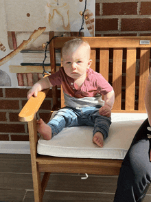 a baby is sitting on a wooden chair with a cushion that says ' cushions ' on it