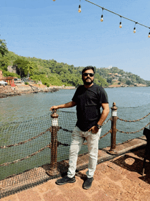 a man in a black shirt stands in front of a fence overlooking a body of water