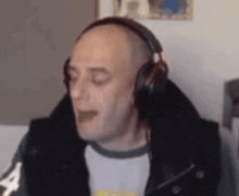 a bald man wearing headphones and a jacket is sitting in front of a computer .