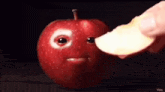a person is holding a slice of apple in front of an apple with a face on it .
