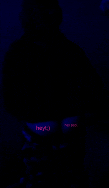 a person is standing in the dark with the words hey papi glowing on their chest .