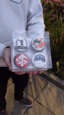 a person is holding a box of cupcakes with the word fisica on one of them