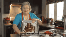 an elderly woman in a blue shirt and orange apron is holding a pan of food with a middle finger drawn on it