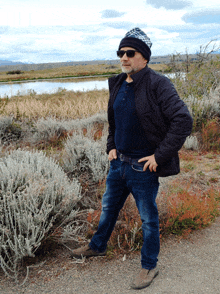 a man wearing sunglasses and a beanie stands in a field