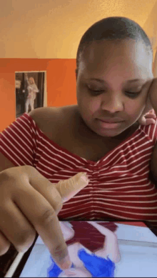 a woman in a red and white striped shirt is looking at a picture on a tablet