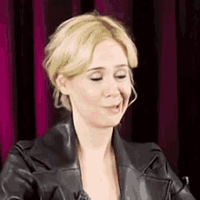 a blonde woman wearing a black leather jacket is making a face