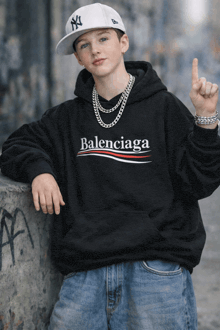 a boy wearing a black balenciaga hoodie and a ny hat