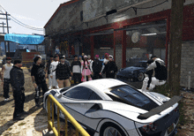 a group of people standing around a white car in front of a building that says united states racing