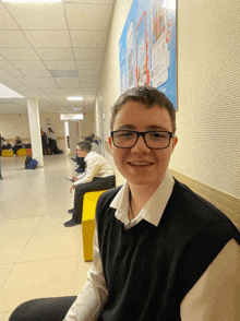 a boy wearing glasses sits in a hallway with a sign that says ' a ' on it