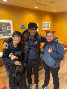 three people posing for a picture in front of a wall that has a sign that says m on it