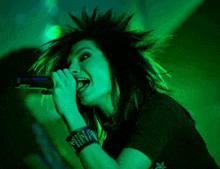 a woman singing into a microphone with green light behind her