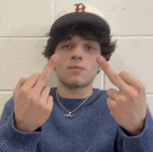 a young man wearing a hat with the letter b on it is giving the middle finger