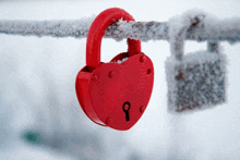 a red heart shaped padlock with a key hanging from a snowy fence