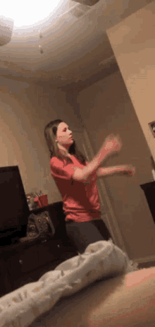 a woman in a red shirt is standing in a bedroom with her arms outstretched .