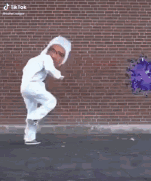 a man in a white suit is walking in front of a brick wall with a picture of a virus on it .