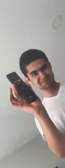 a young man in a white shirt is holding a remote control .