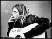 a man smoking a cigarette while holding a guitar with the name kurt cobain on it