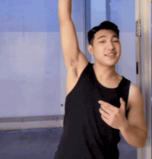 a young man in a black tank top is smiling and raising his arm