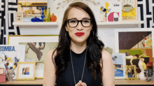 a woman wearing glasses and red lipstick stands in front of a shelf with pictures and a book titled bomba