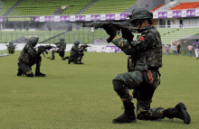 a group of soldiers are kneeling down and holding guns in front of a stadium that has a banner that says cwc