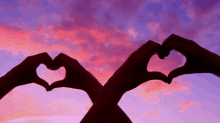 a couple making a heart shape with their hands against a sunset sky