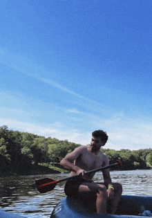 a shirtless man is sitting in a boat with a paddle