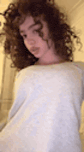 a woman with curly hair is wearing a white shirt and standing in front of a mirror .