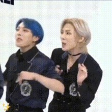 a man and a woman are standing next to each other . the man has blue hair and the woman has blonde hair .