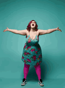 a woman in a blue floral dress and pink tights is standing with her arms outstretched