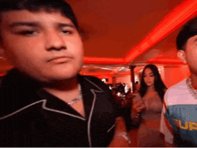 a group of people are standing in a room with red lights . one of the men is looking at the camera .