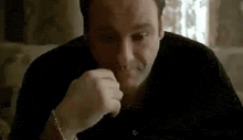 a man in a black shirt is sitting at a table with his hand on his chin .