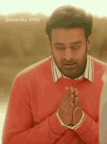 a man wearing a red sweater and a white shirt is praying with his hands together .