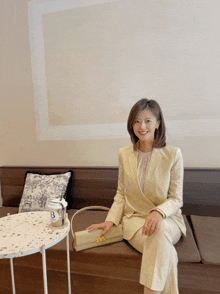 a woman in a suit sits on a couch next to a table with a coffee cup that says bi on it