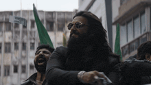 a man with a beard and sunglasses holds a green flag in front of a building