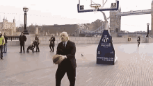 a man in a suit and tie is playing basketball in front of a basketball hoop that says basketball is on london