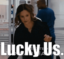 a woman in a black jacket is standing in front of a sign that says " lucky us "