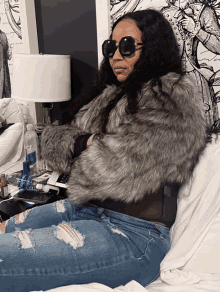 a woman wearing sunglasses is sitting on a bed with a bottle of aquafina water in the background