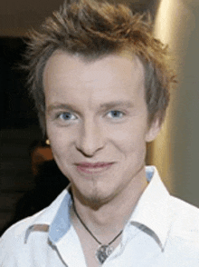 a young man wearing a white shirt and a necklace is smiling for the camera