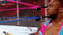 a man in a pink and blue outfit is standing in a wrestling ring .