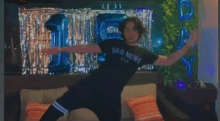 a man wearing a bad news shirt is dancing on a couch in front of balloons .