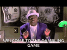 a man in a purple suit and hat is sitting in front of a green lamp and says welcome to the gambling game .