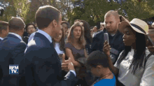 a man in a suit shakes hands with a young boy in front of a crowd with bfm tv written on the bottom right