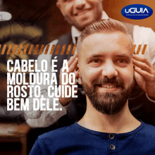 a man with a beard is getting his hair cut by a barber with a uguia logo in the background