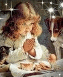 a little girl is praying while sitting at a table with a dog