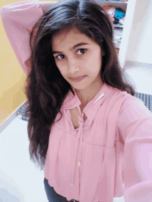 a woman in a pink shirt is taking a selfie with her hand in her hair