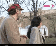 a man in a plaid hat is talking to a woman in a park with a sign that says zabava on the bottom